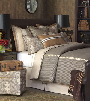 Traditional library style bedroom with houndstooth patterned bedding, pillows, and a suitcase on an ottoman.
