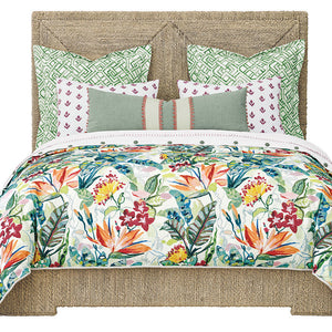 A bed styled with a colorful tropical floral comforter, patterned accent pillows, and a woven jute headboard and footboard against a white background.