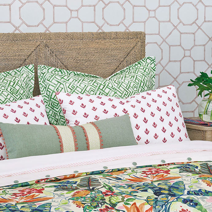 A bed dressed in a tropical floral comforter and matching pillows, styled in a bedroom with wood nightstands, a patterned wallpaper background, a hanging lamp, and a rug.