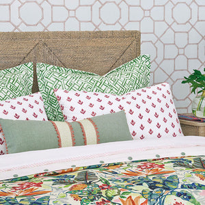 A styled bed with multiple decorative pillows and a colorful floral duvet cover, set against a patterned wallpaper and a woven headboard.