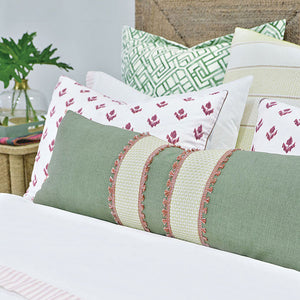 Decorative pillows arranged on a bed, including a sage green long bolster pillow with light mint bands and coral fringed gimp trim, white pillows with berry color floral print, and a kelly green trellis pattern Euro pillow.